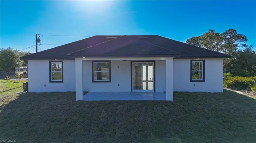 Rear view of house featuring a yard, stucco siding, a patio, and roof with shingles