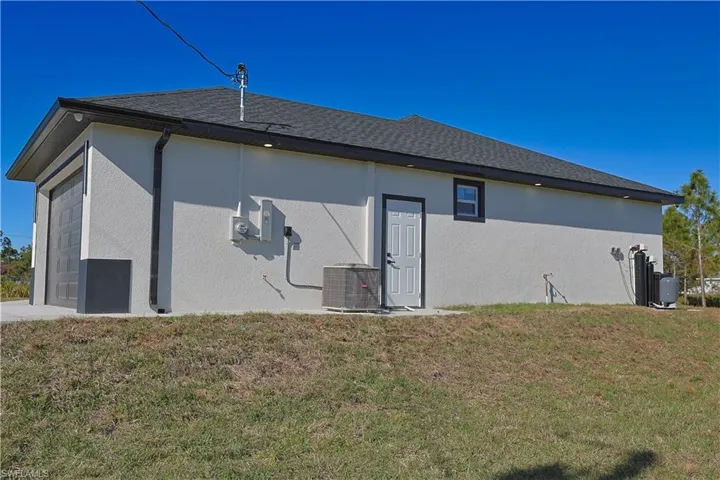 Back of house with a yard, central AC unit, a garage, and stucco siding