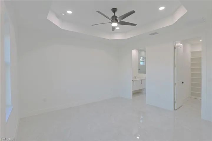 Unfurnished bedroom with a tray ceiling, ensuite bath, recessed lighting, baseboards, and a spacious closet