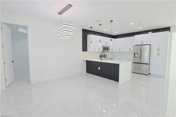 Kitchen with pendant lighting, light countertops, appliances with stainless steel finishes, white cabinets, and a sink