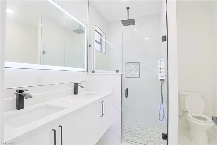 Full bath with a marble finish shower, double vanity, toilet, and a sink