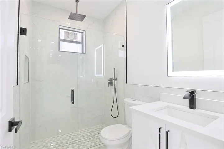 Full bath with vanity, a marble finish shower, tile walls, toilet, and backsplash