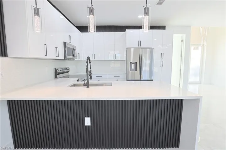 Kitchen with pendant lighting, light countertops, a peninsula, stainless steel appliances, and a sink