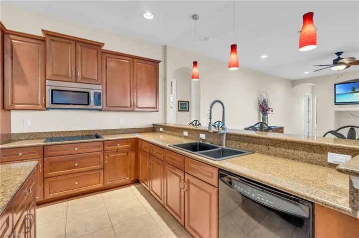 Kitchen featuring light stone counters, black appliances, ceiling fan, sink, and decorative light fixtures
