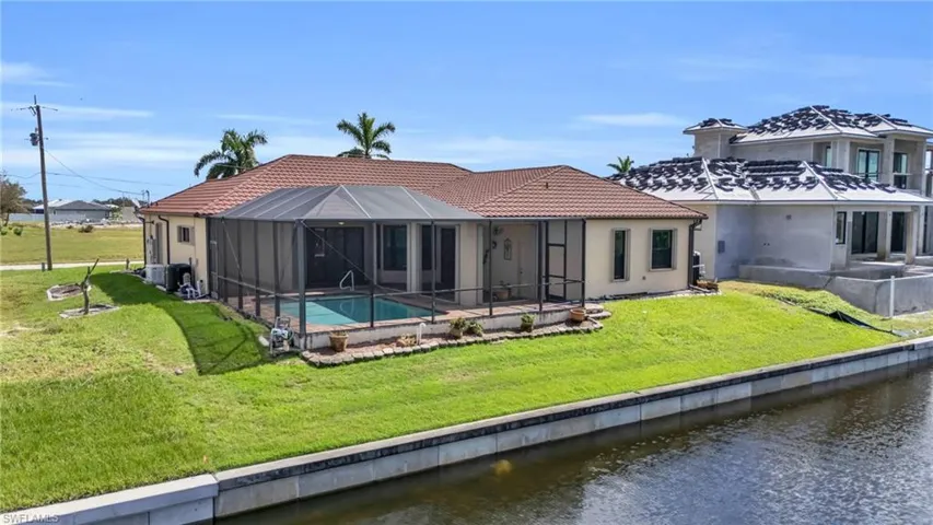 Rear view of property featuring a lanai, screen enclosure, a water view, and a lawn