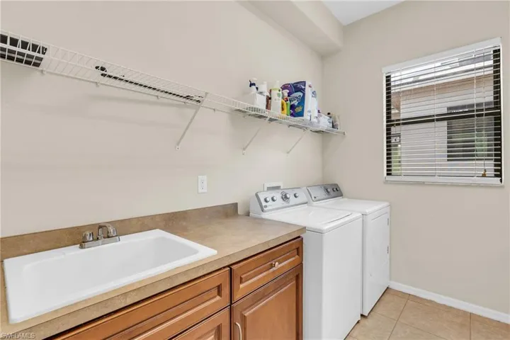 Clothes washing area with light tile patterned flooring, independent washer and dryer, sink, and cabinets