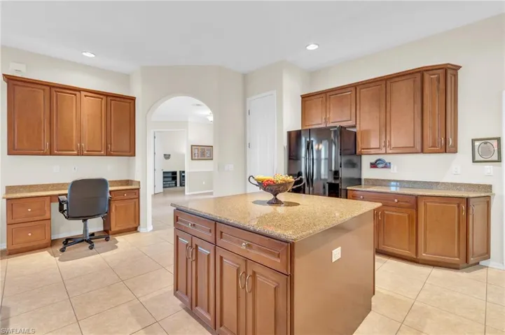 Kitchen featuring light stone counters, built in desk, a center island, black fridge, and light tile floors