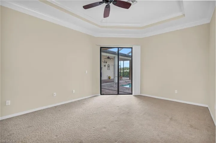 Carpeted owner's bedroom featuring ceiling fan, a tray ceiling, and ornamental molding