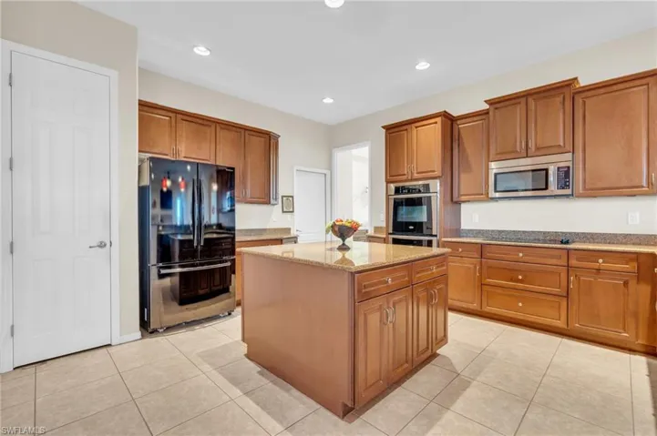 Kitchen featuring light stone counters, appliances with stainless steel finishes, light tile floors, and a kitchen island
