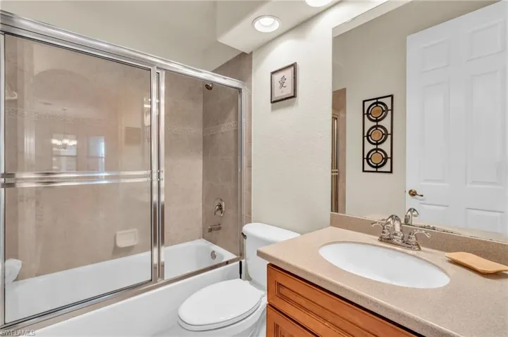 Full bathroom with enclosed tub / shower combo, vanity, and toilet