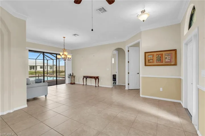 Tiled spare room with ceiling fan with notable chandelier and crown molding