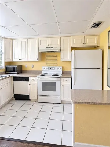 Kitchen featuring white cabinetry, white tile flooring, light-toned countertops, and white appliances