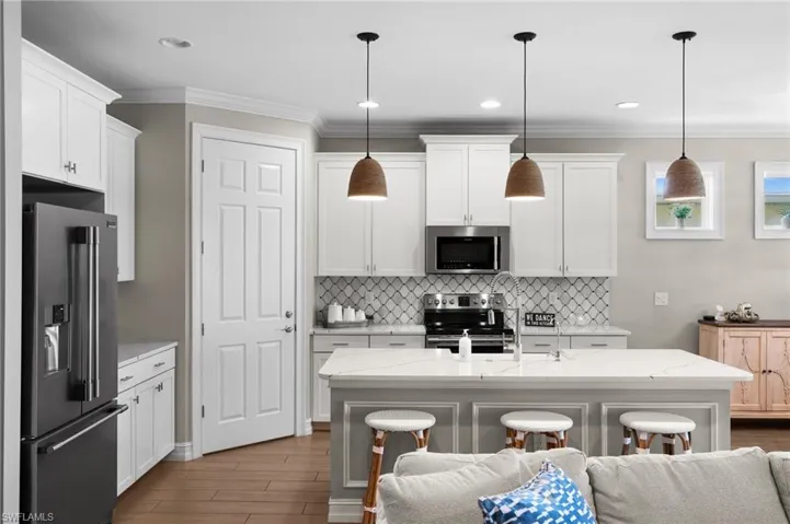 Kitchen featuring a center island with sink, pendant lighting, white cabinetry, and stainless steel appliances