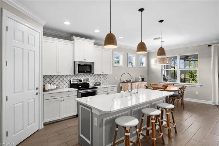 Kitchen featuring hanging light fixtures, stainless steel appliances, an island with sink, a kitchen bar, and white cabinets