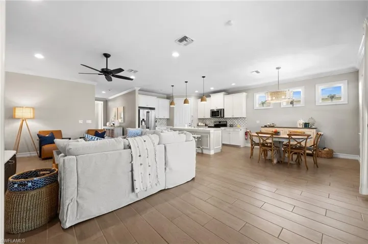 Living room with ceiling fan, ornamental molding, and light wood-type flooring