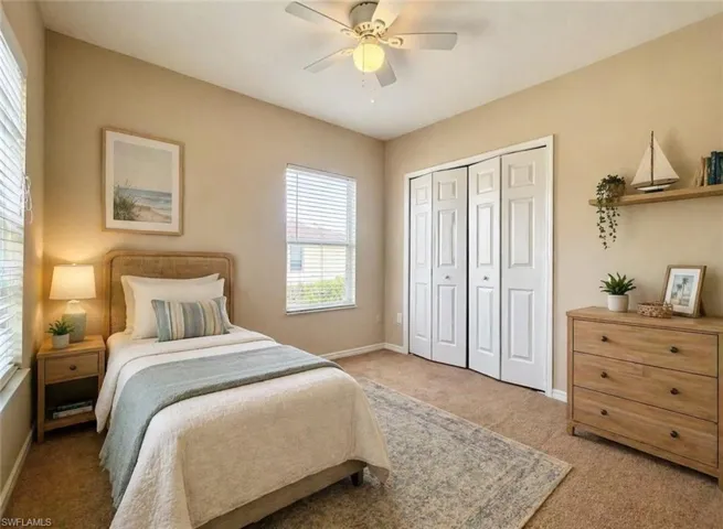 Neutral-toned room featuring a ceiling fan with integrated lighting, two windows with blinds, bi-fold closet doors, and wood-finish flooring