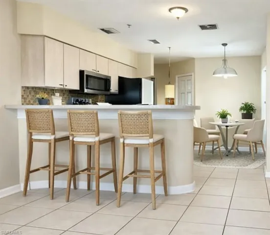 Open-concept kitchen featuring light-toned cabinetry, stainless steel microwave, and a breakfast bar with a light-colored countertop