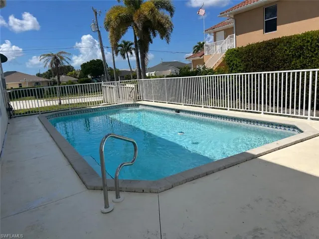 Outdoor swimming pool featuring a tiled waterline, surrounding concrete patio, and white perimeter fencing