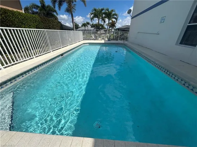 Outdoor swimming pool featuring a patterned tile border and surrounding white fencing
