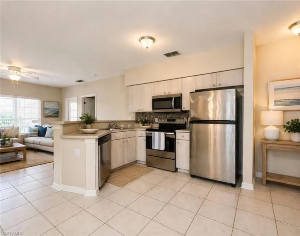 Open-concept kitchen featuring light-toned cabinetry, stainless steel appliances, and a mosaic tile backsplash