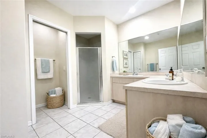 Bathroom featuring a dual vanity with integrated sinks, a large wall-mounted mirror, and a glass-enclosed shower