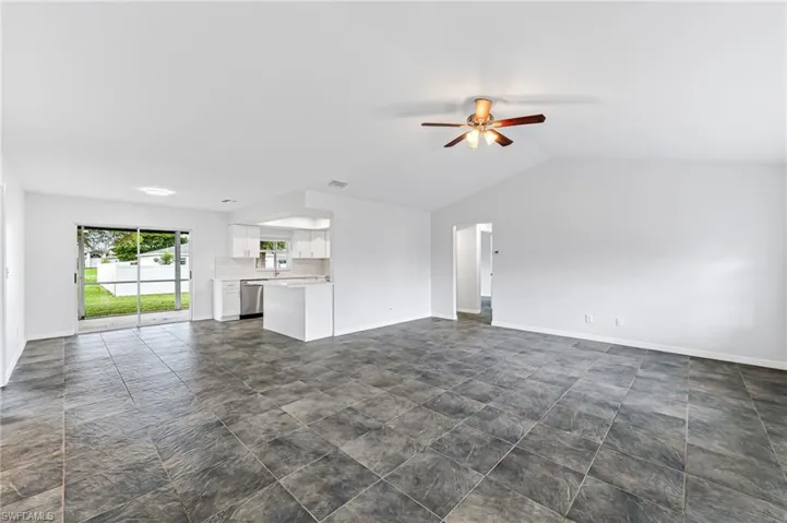 Unfurnished living room featuring ceiling fan, dark tile patterned flooring, and vaulted ceiling