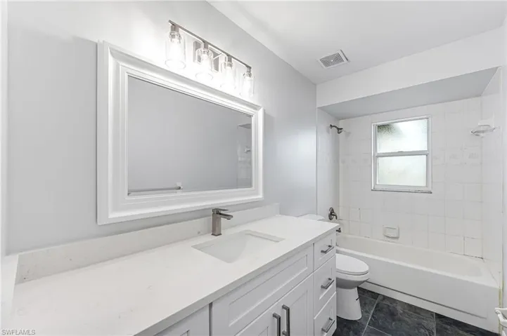 Full bathroom with tile patterned floors, vanity, tiled shower / bath combo, and toilet