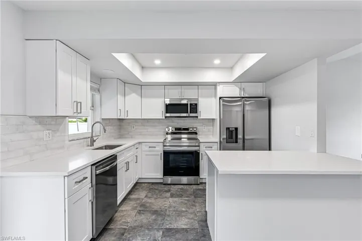 Kitchen with dark tile patterned flooring, stainless steel appliances, backsplash, white cabinets, and sink
