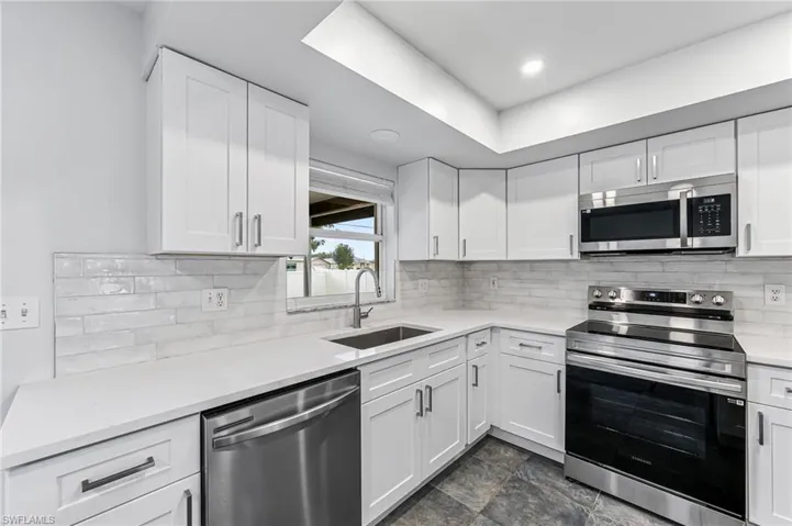 Kitchen with white cabinets, sink, stainless steel appliances, and dark tile patterned flooring