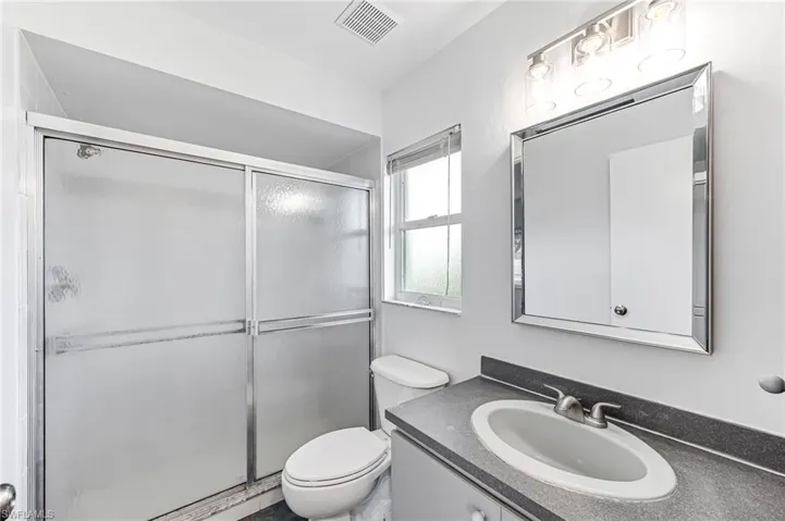 Bathroom featuring a shower with door, toilet, and vanity