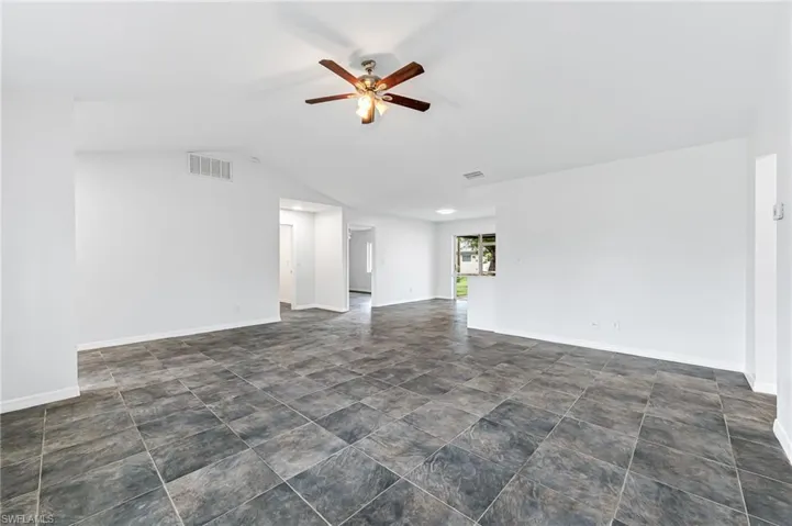 Spare room with ceiling fan, dark tile patterned floors, and lofted ceiling