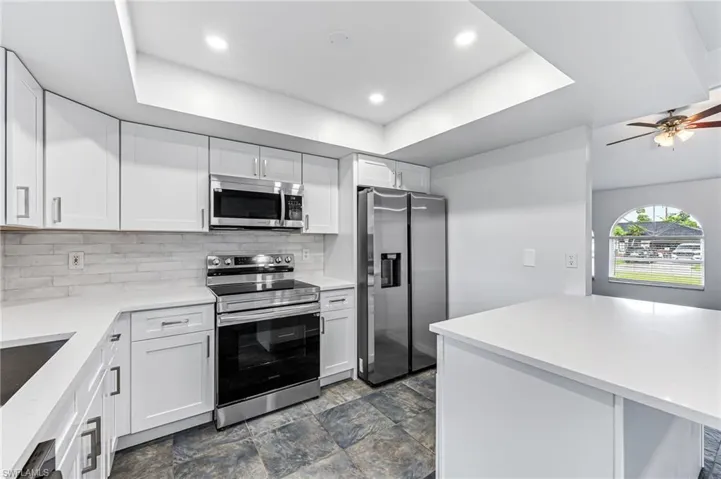 Kitchen with stainless steel appliances, backsplash, white cabinetry, dark tile patterned floors, and ceiling fan