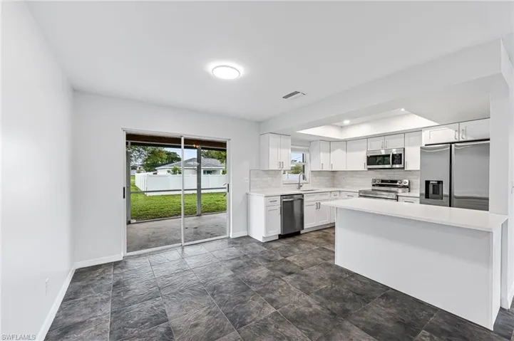 Kitchen with appliances with stainless steel finishes, dark tile patterned floors, sink, and white cabinetry