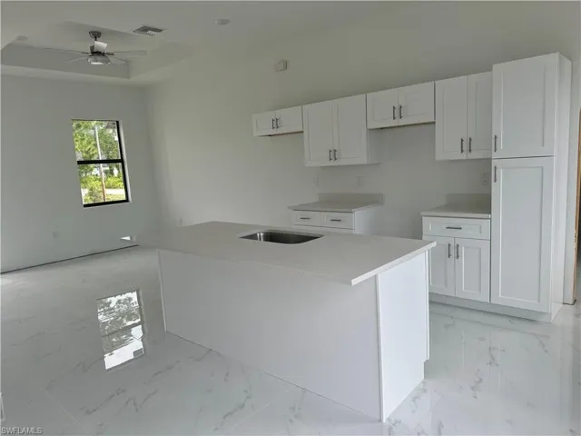 Kitchen with an island with sink, white cabinetry, light tile flooring, and ceiling fan