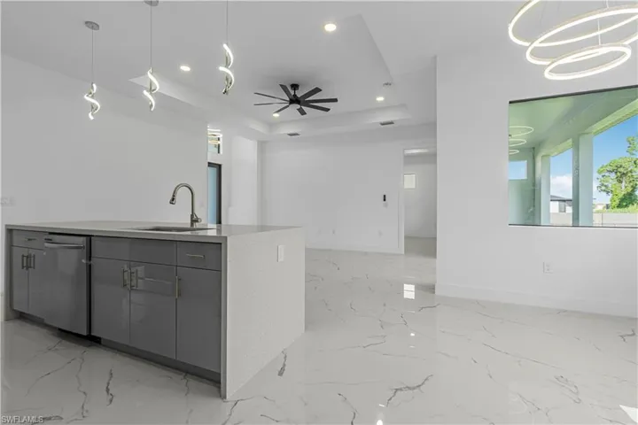 Kitchen with gray cabinetry, open floor plan, a tray ceiling, light marble finish floors, and recessed lighting