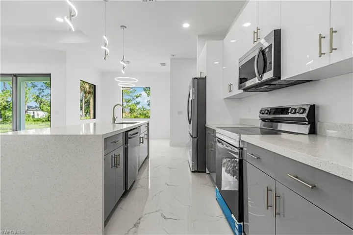 Kitchen with appliances with stainless steel finishes, modern cabinets, light marble finish flooring, gray cabinets, and a center island with sink