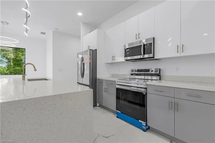 Kitchen featuring appliances with stainless steel finishes, light marble finish floors, decorative light fixtures, white cabinetry, and recessed lighting