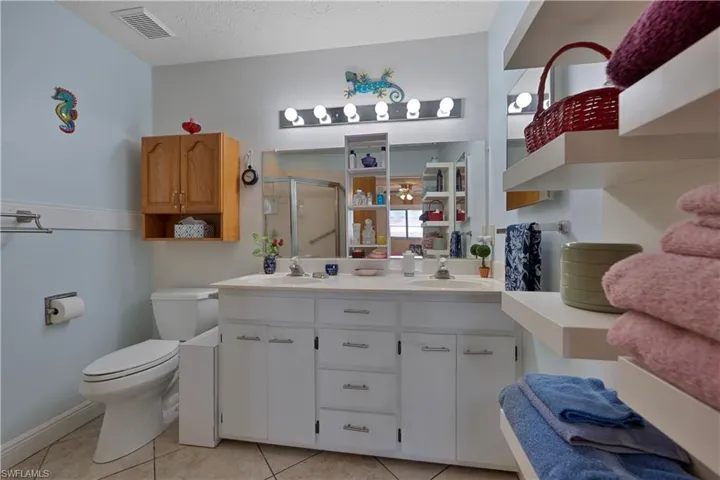 Full bath featuring double vanity, a shower stall, light tile patterned flooring, and a textured ceiling