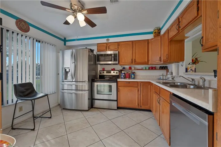 Kitchen with appliances with stainless steel finishes, light countertops, light tile patterned floors, brown cabinets, and ceiling fan