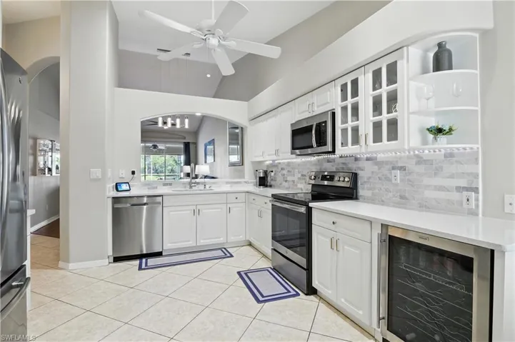 Kitchen with arched walkways, appliances with stainless steel finishes, beverage cooler, backsplash, and lofted ceiling