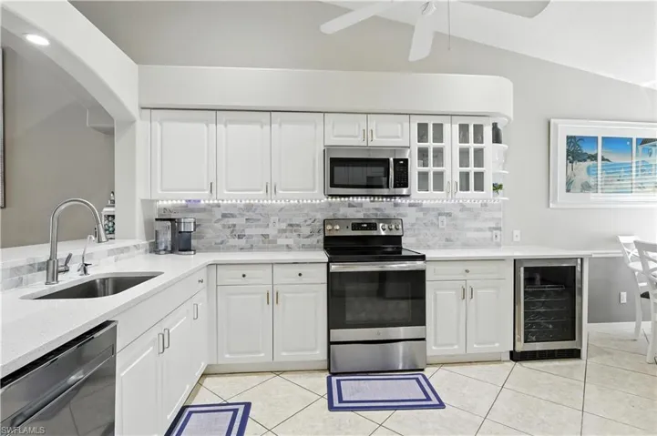 Kitchen featuring beverage cooler, stainless steel appliances, tasteful backsplash, light stone counters, and vaulted ceiling