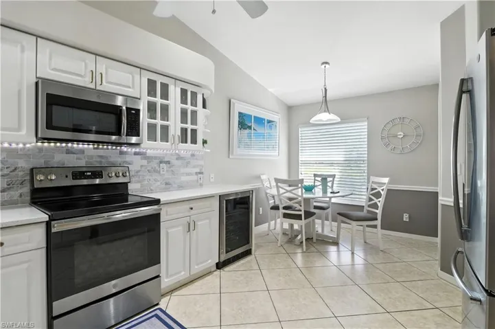 Kitchen featuring stainless steel appliances, tasteful backsplash, light tile patterned floors, vaulted ceiling, and white cabinets