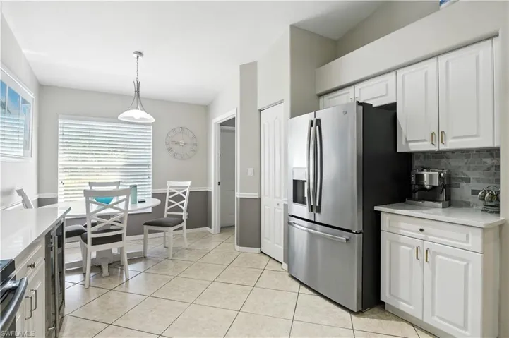 Kitchen featuring stainless steel refrigerator with ice dispenser, light stone counters, white cabinets, backsplash, and pendant lighting