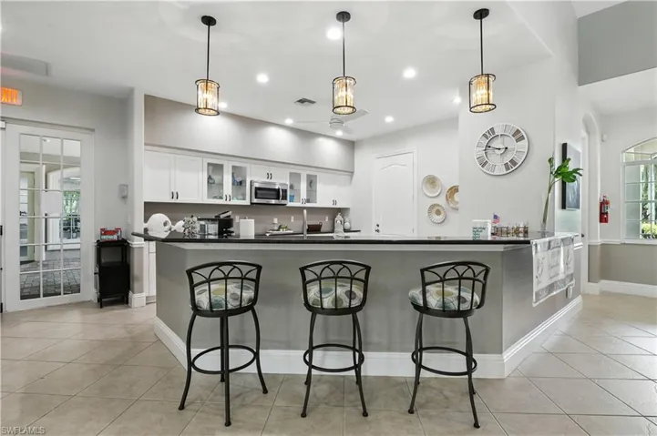 Kitchen with light tile patterned floors, glass insert cabinets, white cabinets, decorative light fixtures, and a breakfast bar