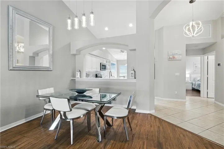 Dining room with wood finished floors, arched walkways, a chandelier, a ceiling fan, and high vaulted ceiling