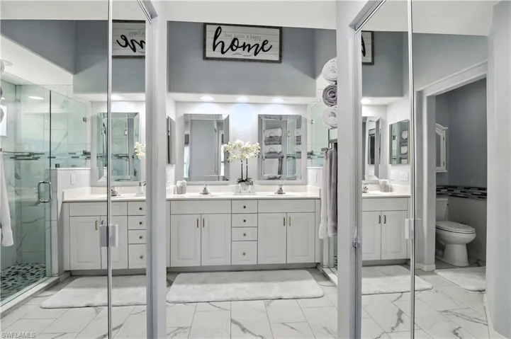 Bathroom featuring double vanity, a marble finish shower, and light marble finish flooring
