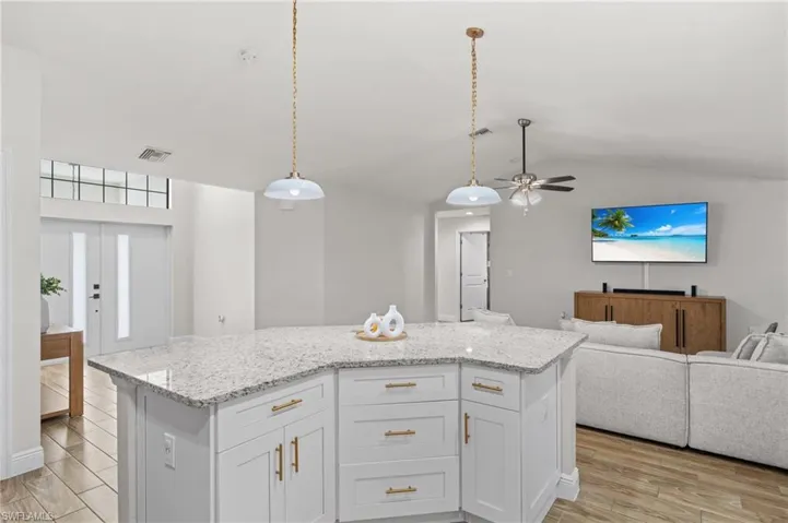 Kitchen with ceiling fan, a kitchen island, pendant lighting, vaulted ceiling, and white cabinets