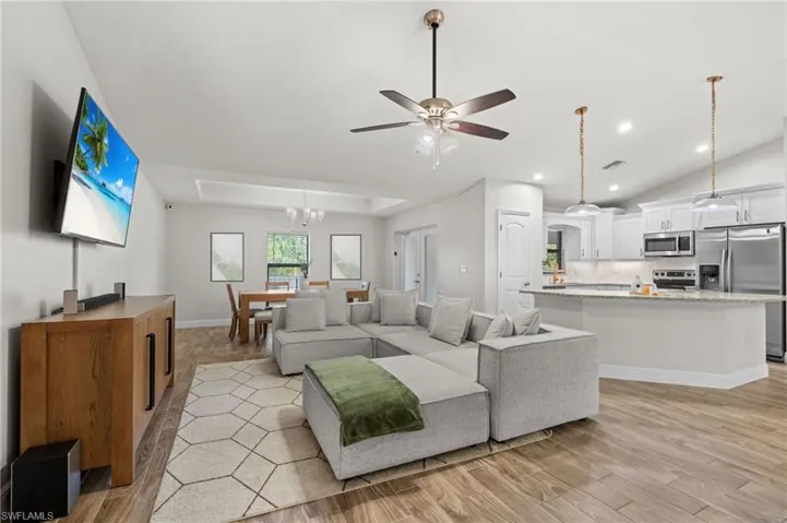 Living room featuring ceiling fan with notable chandelier and light wood-type flooring