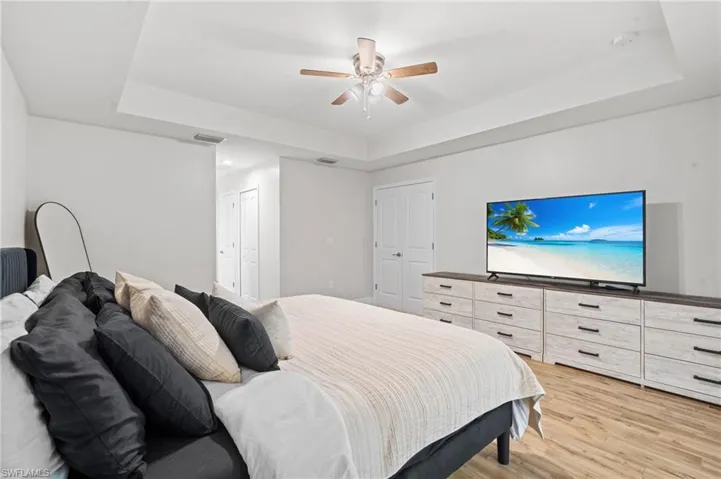 Bedroom with ceiling fan, a raised ceiling, and light hardwood / wood-style flooring