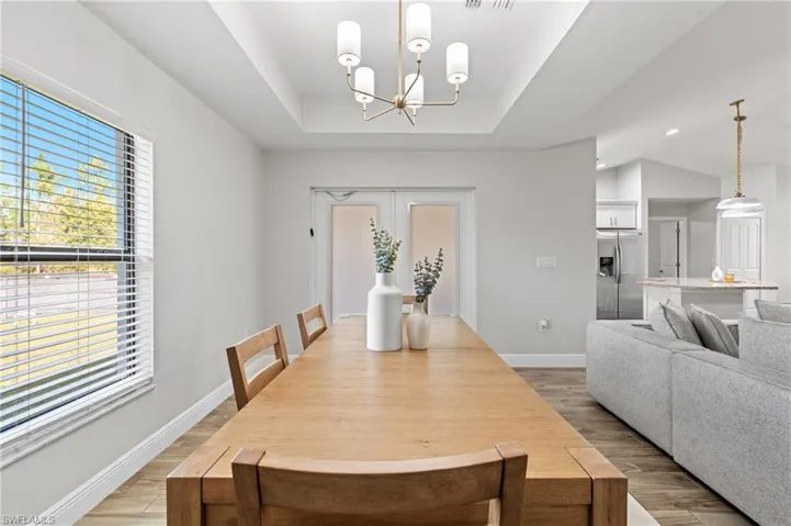 Dining room featuring a tray ceiling, light hardwood / wood-style flooring, a chandelier, and french doors